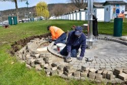 Zwei Männer pflastern den Boden rund um die Duschen im Strandbad